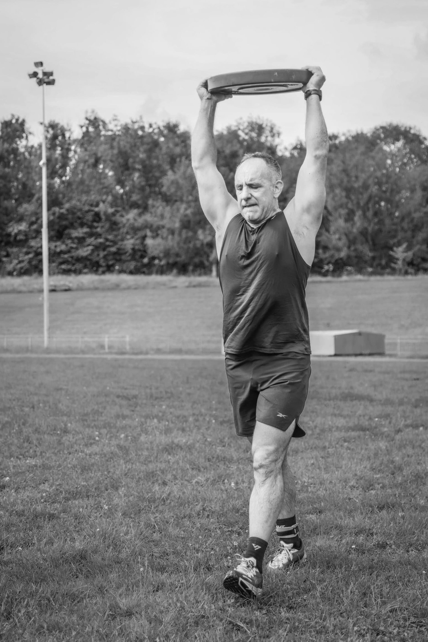 Atleta che trasporta un disco da pesi sopra la testa nell'esercizio "Overhead Carry Labour"